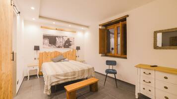 Une chambre à coucher comprenant un lit, un banc en bois, une commode, une chaise et une fenêtre avec un cadre en bois.
