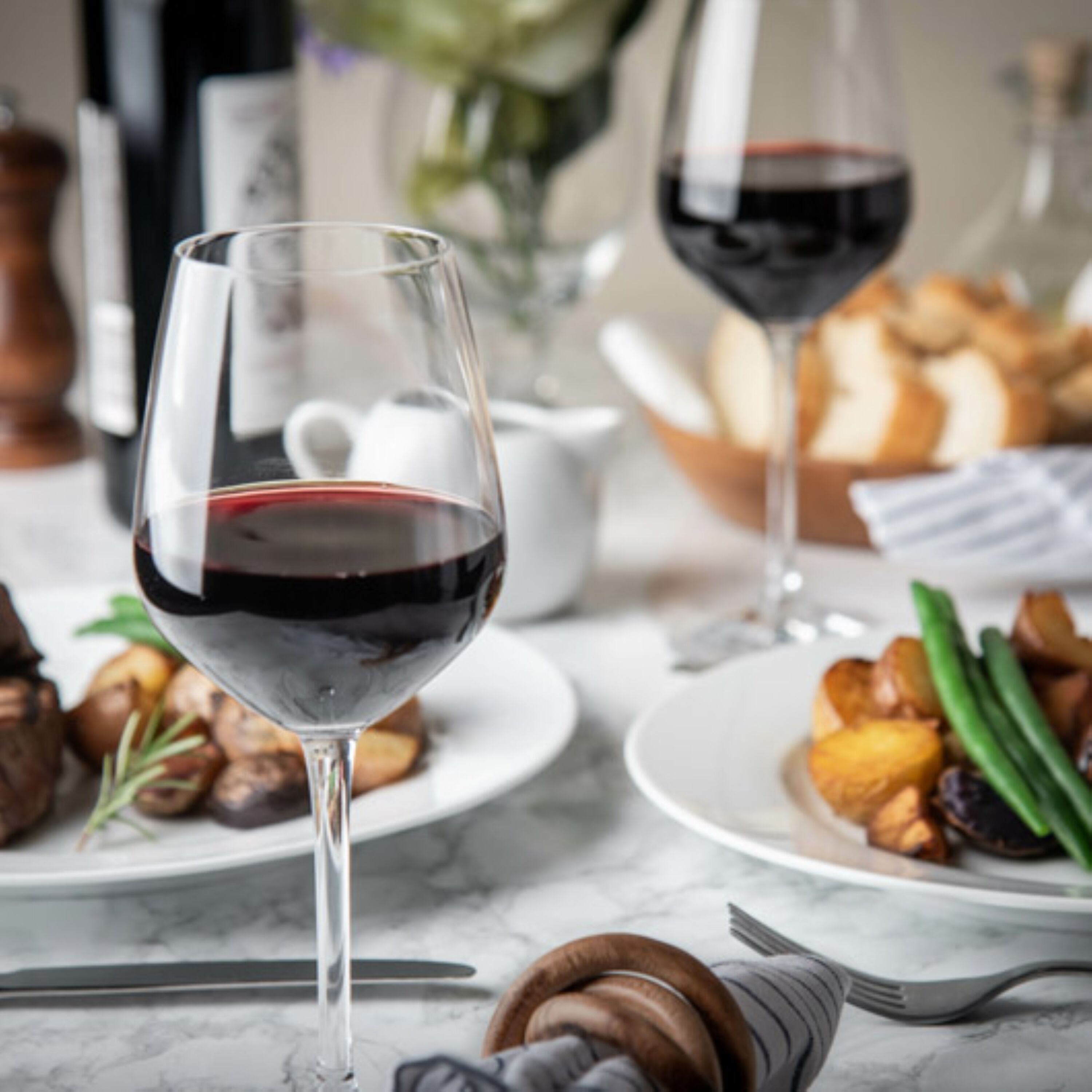 A dining table with plates of food, two wine glasses, and a teapot.