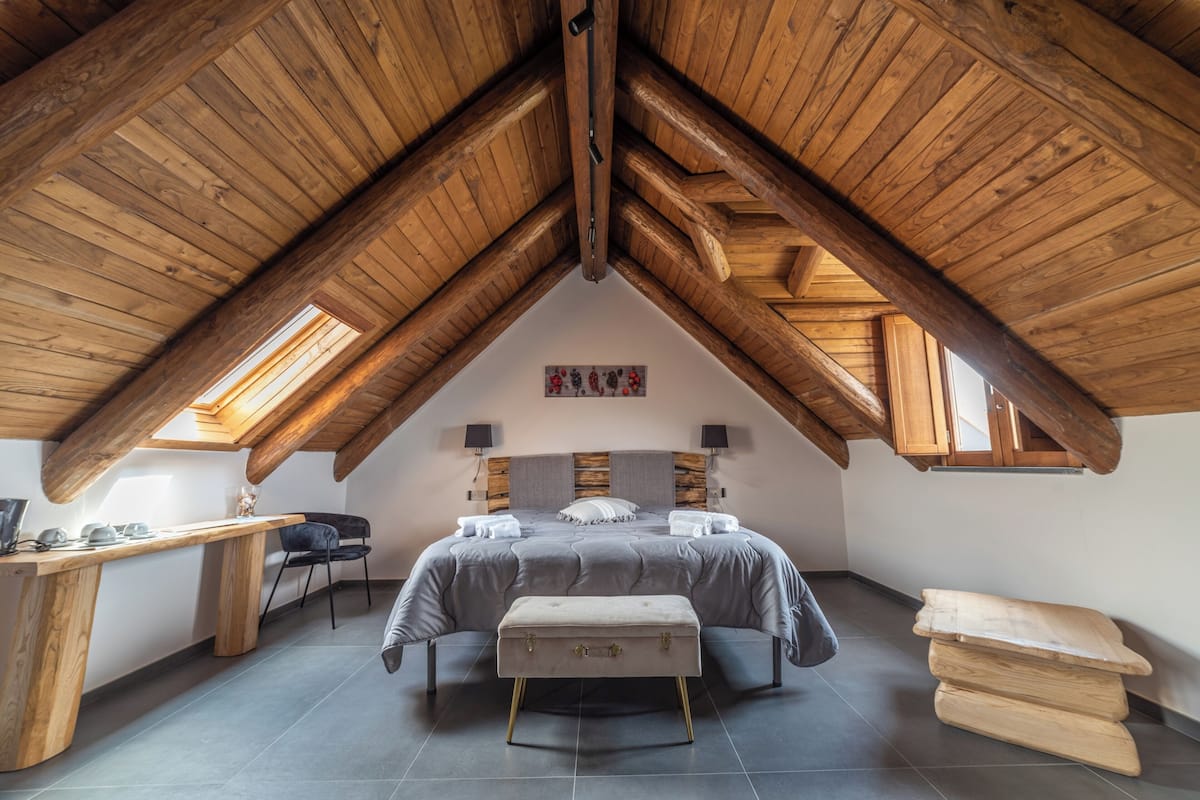 Un dormitorio con techo inclinado, cama, escritorio y silla.