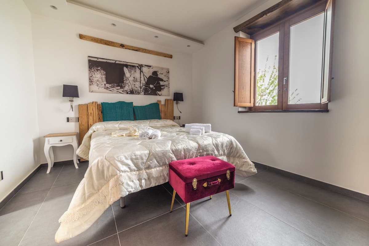 Un dormitorio con una cama, mesitas de noche, una ventana y un cuadro en la pared.