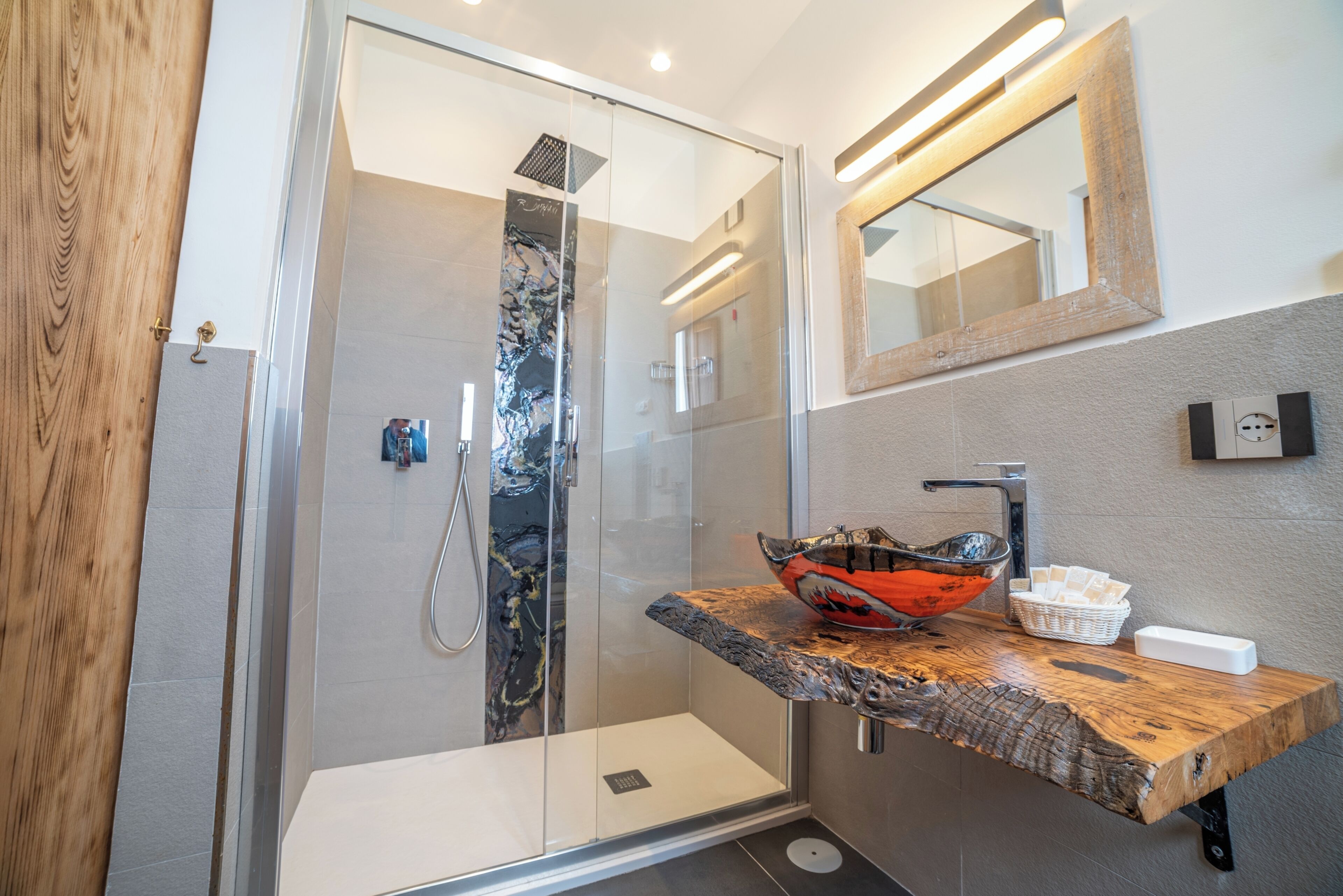 A modern bathroom with a glass-enclosed shower, a wooden vanity with a large bowl sink, and a mirror above the sink.