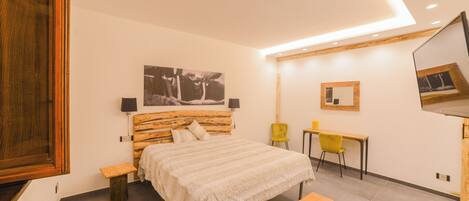 Un dormitorio moderno con una cama de madera, mesitas de noche, un banco, un escritorio y sillas.