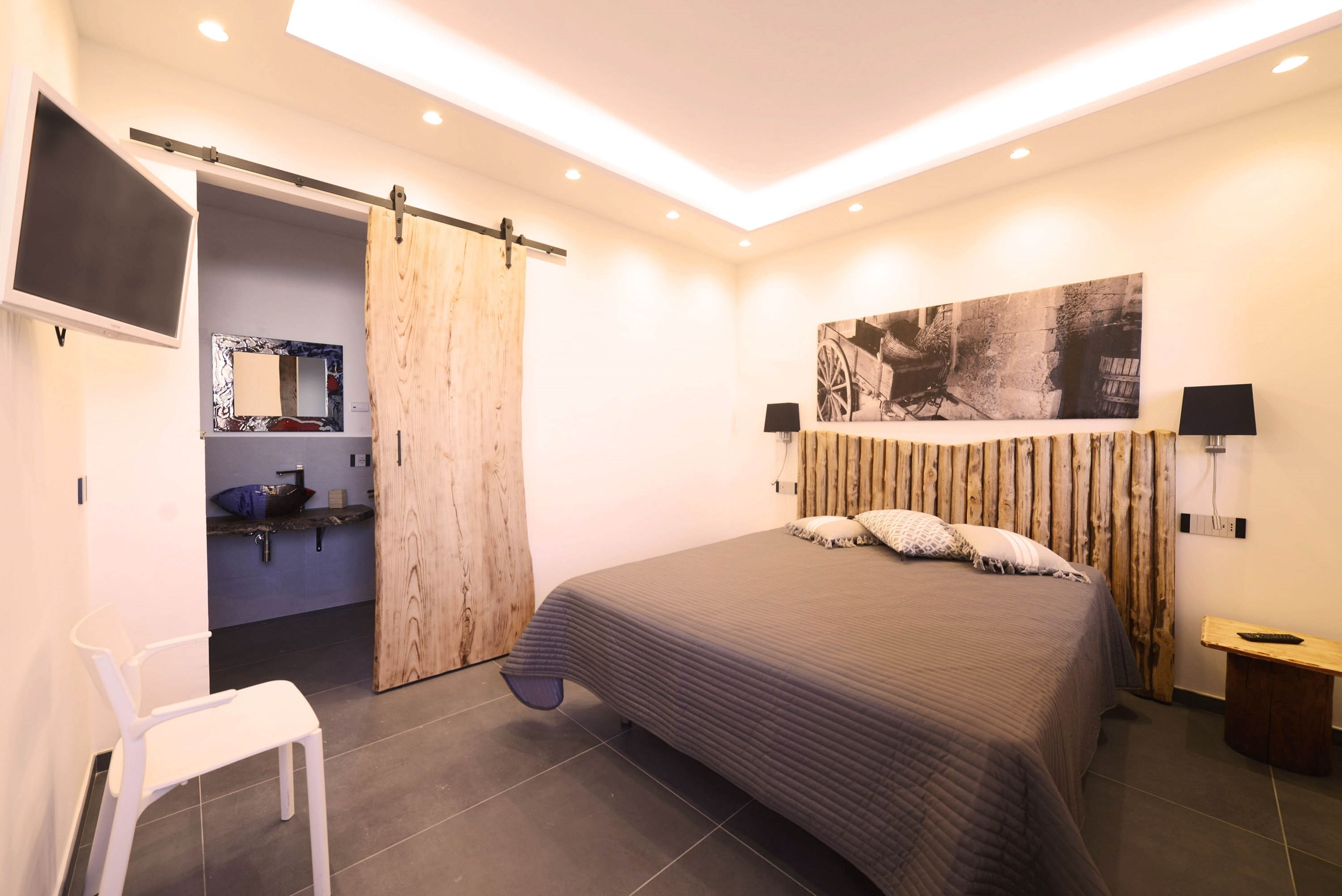 Een moderne slaapkamer met een groot bed, een inloopkast met schuifdeuren, een tv aan de muur en een houten hoofdbord.