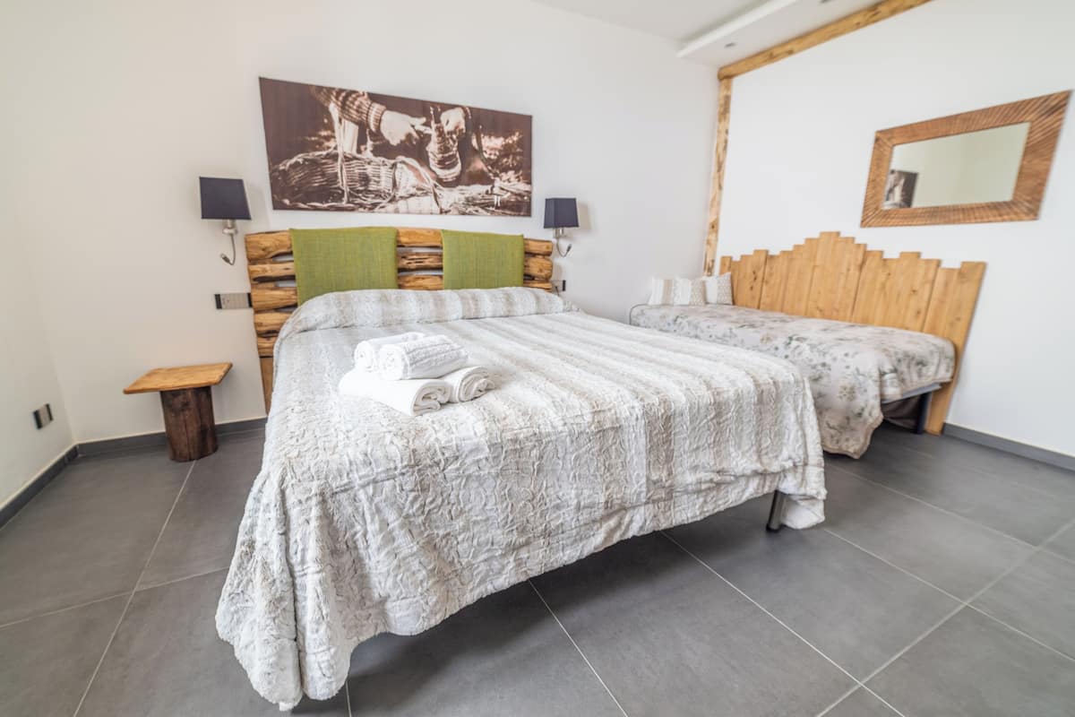 Un dormitorio con dos camas, cabeceros de madera, un taburete pequeño de madera y un espejo fijado a la pared.