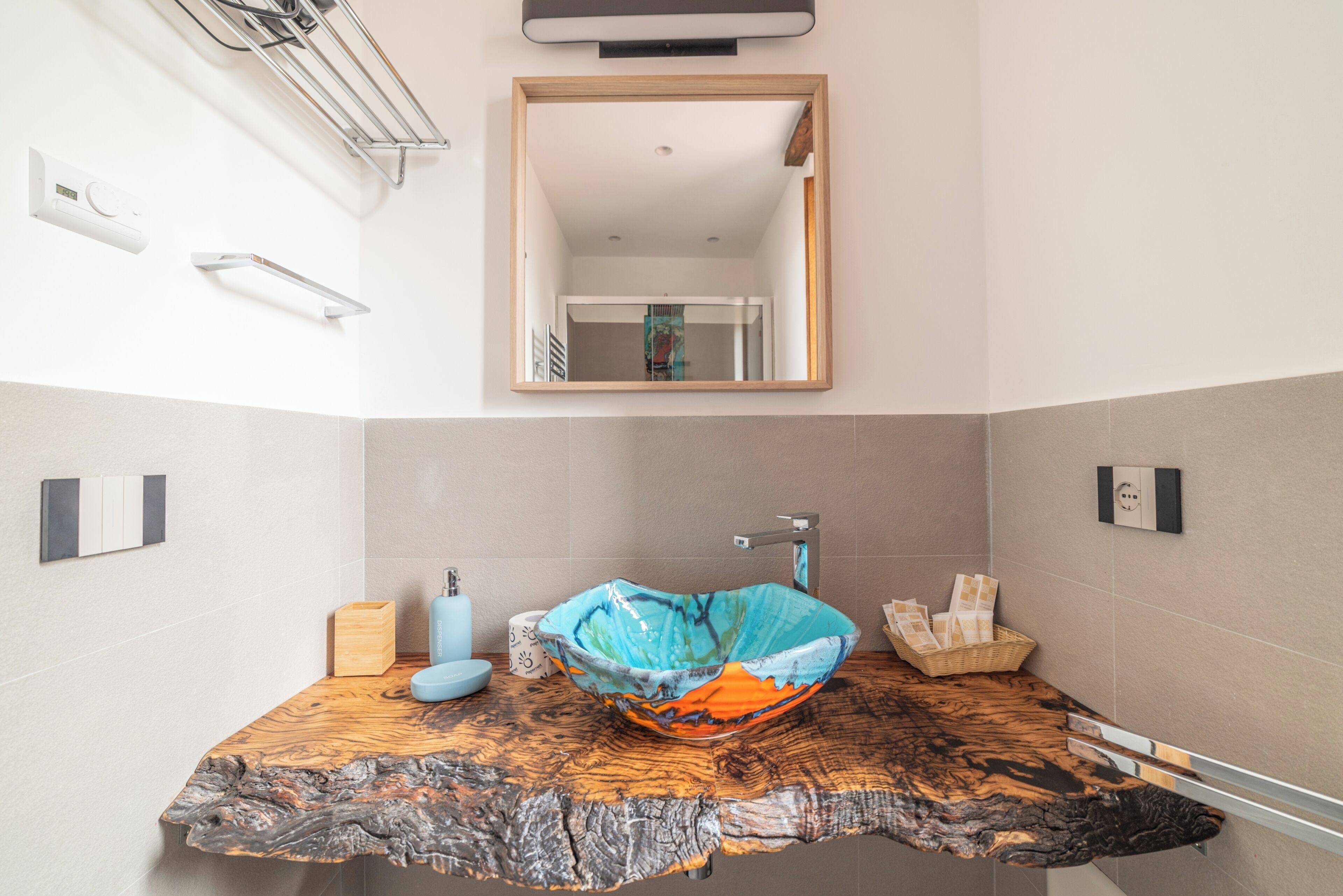 Une salle de bain avec un plan de toilette en bois, un lavabo en forme de bol en verre aux couleurs vives et un miroir au-dessus.