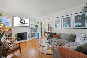 A modern living room with a fireplace, a sofa, a coffee table, and framed pictures on the wall. - Entertainer - Brookside + Walkable + Firepit (Kansas City)