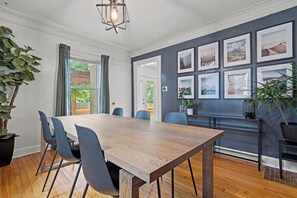 A dining area with a wooden table and chairs, a dark wall with framed pictures, and a plant on the left. - Entertainer - Brookside + Walkable + Firepit (Kansas City)