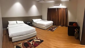 A hotel room with a large bed, a smaller bed, a desk, a chair, a sofa, and a curtain.