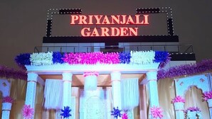 The entrance of Priyanjali Garden with a large illuminated sign and decorative floral arrangements.