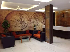 Rebedor amb un mural gran de mapa mundial, una taquilla d'estació i una zona d'estar amb sofàs i una taula de cafè.