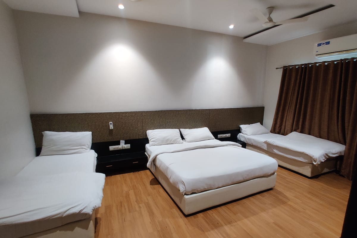 Een hotelkamer met drie op een rij staande bedden, een plafondventilator en een airconditioning.