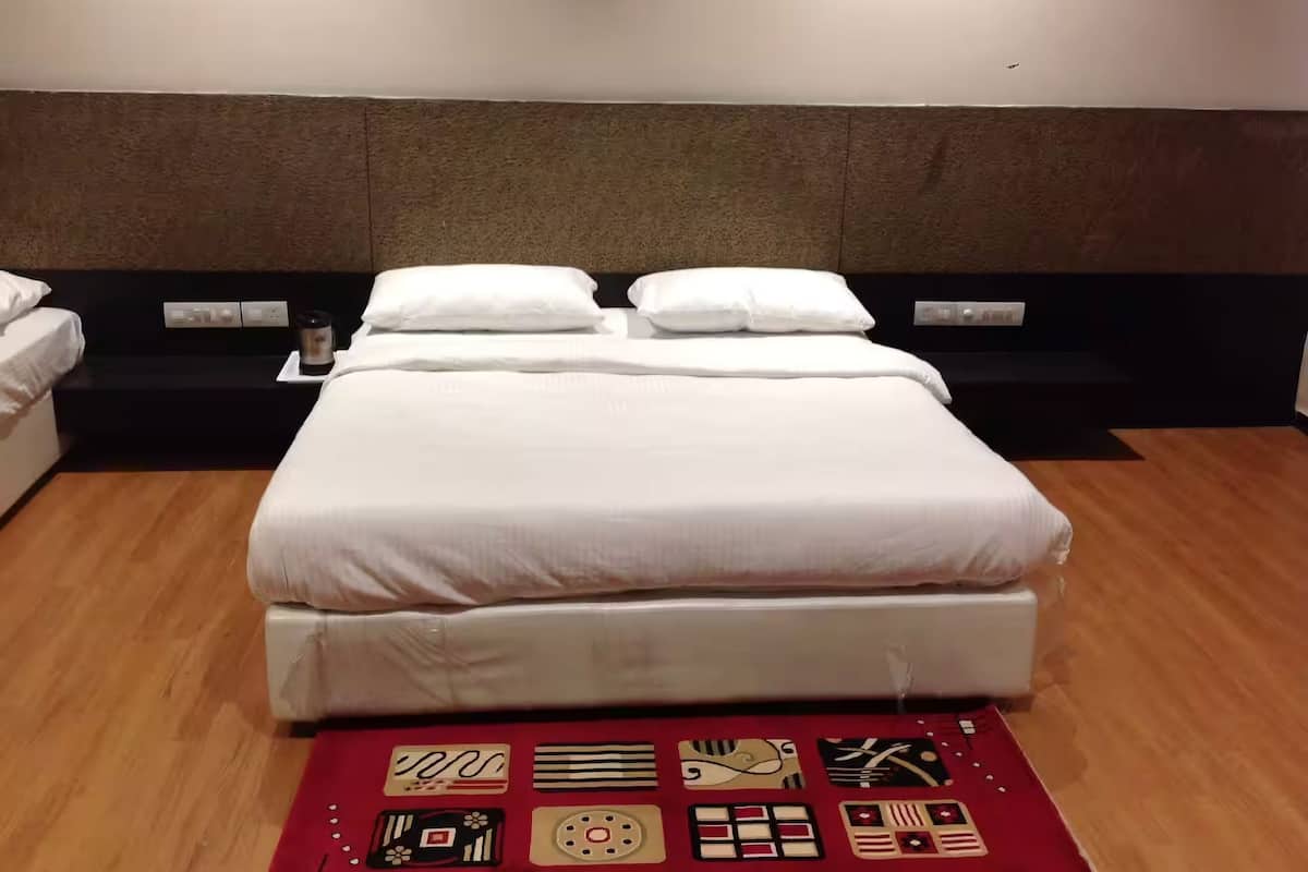 Een net opgemaakt bed met witte lakens, een hoofdbord en een rood decoratief vloerkleed met diverse patronen.