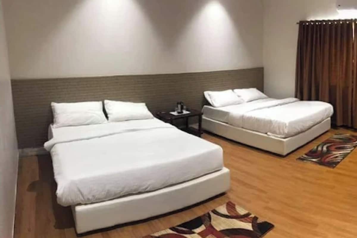 Een hotelkamer met twee eenpersoonsbedden, een houten vloer, een kamerkleed met patroon en een nachtkastje met lamp.