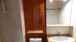 A bathroom with a wooden panel wall, a white toilet, a sink with a mirror above it, and a shower area. - Studio for 4 in Les Saisies, parking (Les Saisies)