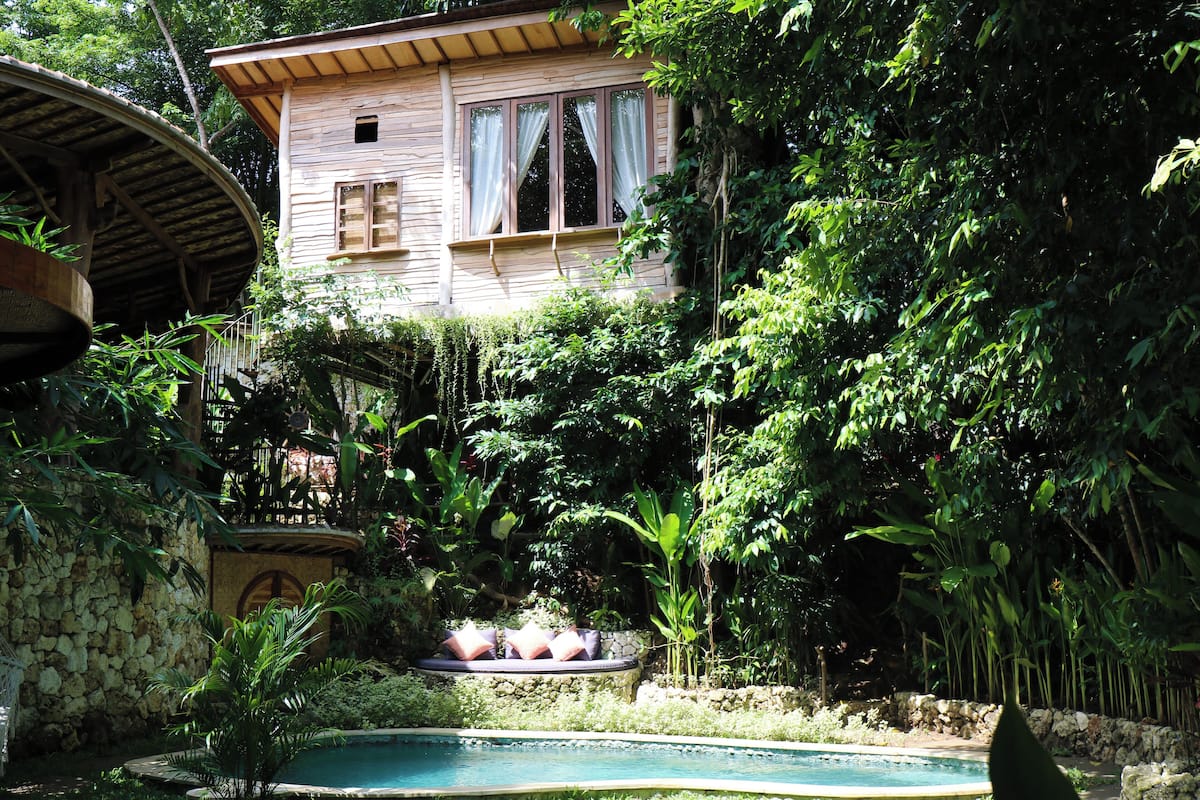 A wooden house with a pool surrounded by lush greenery.