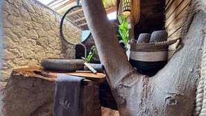 A rustic bathroom with a stone wall, a wooden basin, a towel, and a woven basket.