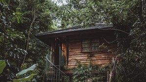 A rustic cabin surrounded by dense foliage, with a spiral staircase leading to the entrance. - Roots Tree House (Ungasan)