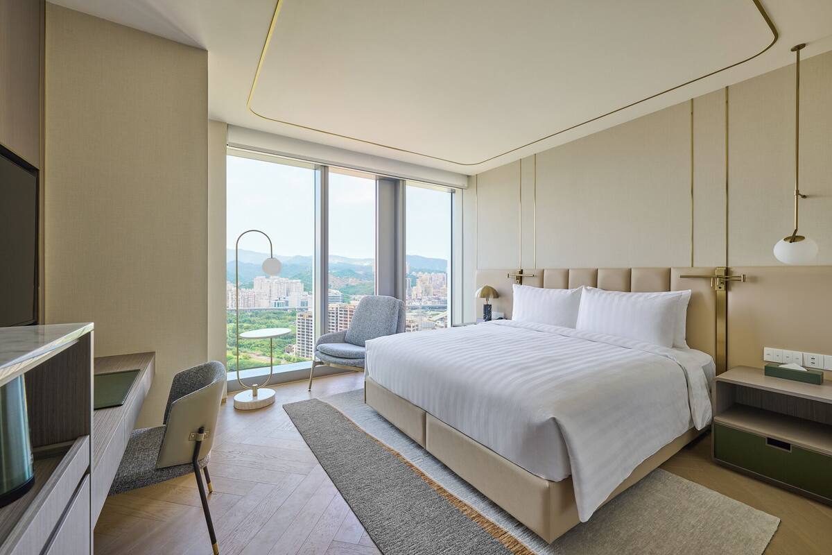 A modern hotel room with a large bed, a desk, and a chair.