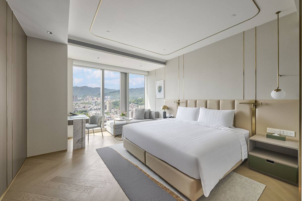 A modern hotel room with a large bed, a desk, and a view of the city.