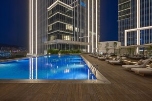 Un hotel moderno con piscina en la azotea, zona de estar y un rascacielos al fondo.