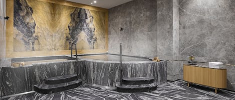 A modern spa area with a marble floor, a large wall-mounted bathtub, and a wooden vanity with towels.