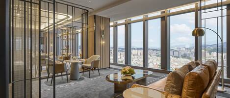 A modern interior with a sofa, coffee table, and dining area, featuring large windows and a city view.