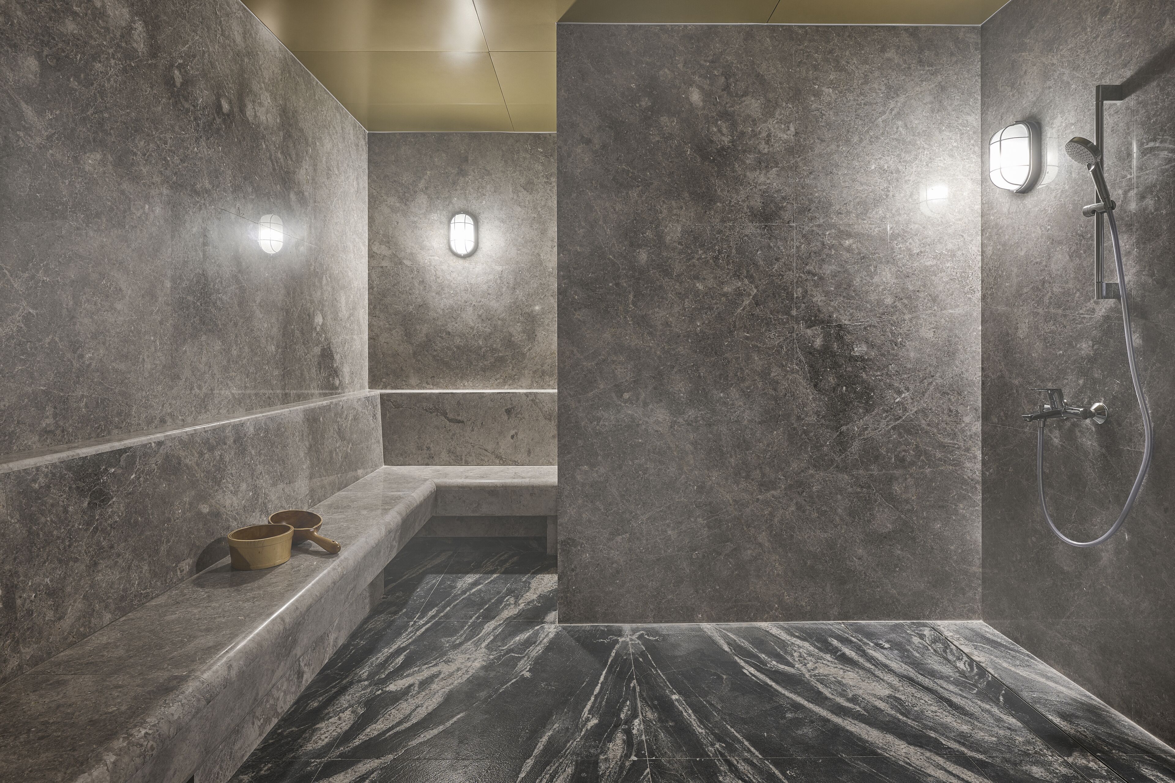 Un baño moderno con ducha de mármol, un banco y lavamanos integrado.