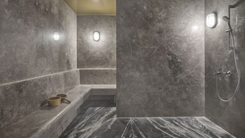 Un baño moderno con ducha de mármol, un banco y lavamanos integrado.
