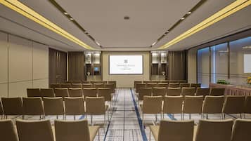 Un salón de conferencias con filas de sillas, una pantalla de proyección mostrando 'GRAND HILAI TAIPEI' y piso alfombrado.