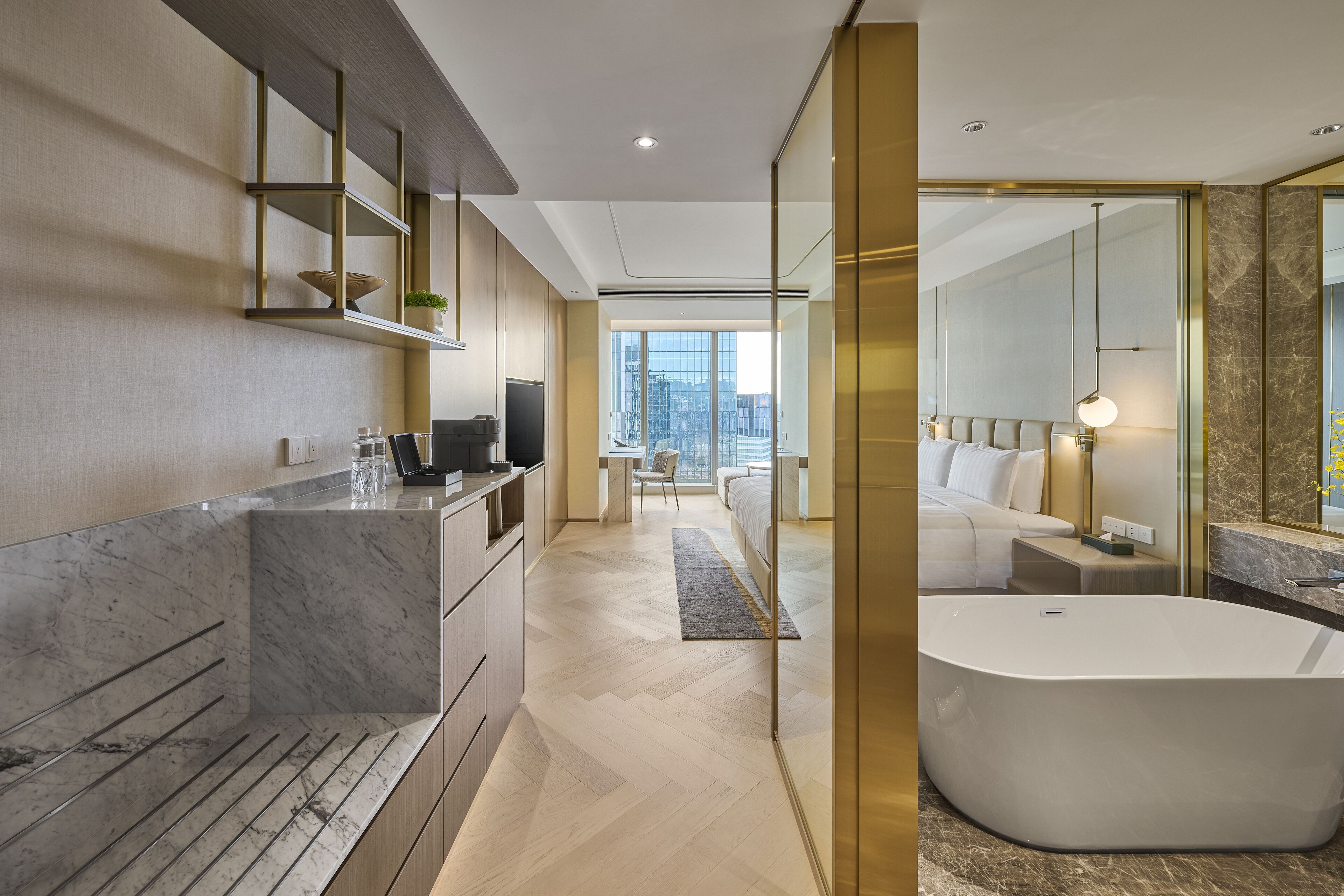 A modern hotel bathroom with a large bathtub, marble countertops, and a city view.