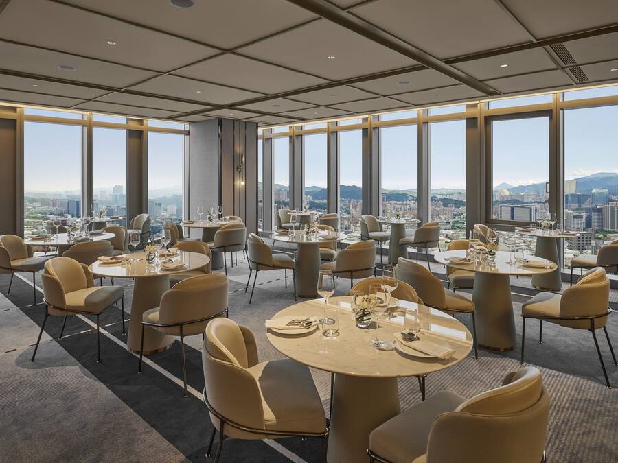 Ein moderner Essbereich mit runden Tischen und Stühlen, große Fenster mit Blick auf die Stadt.