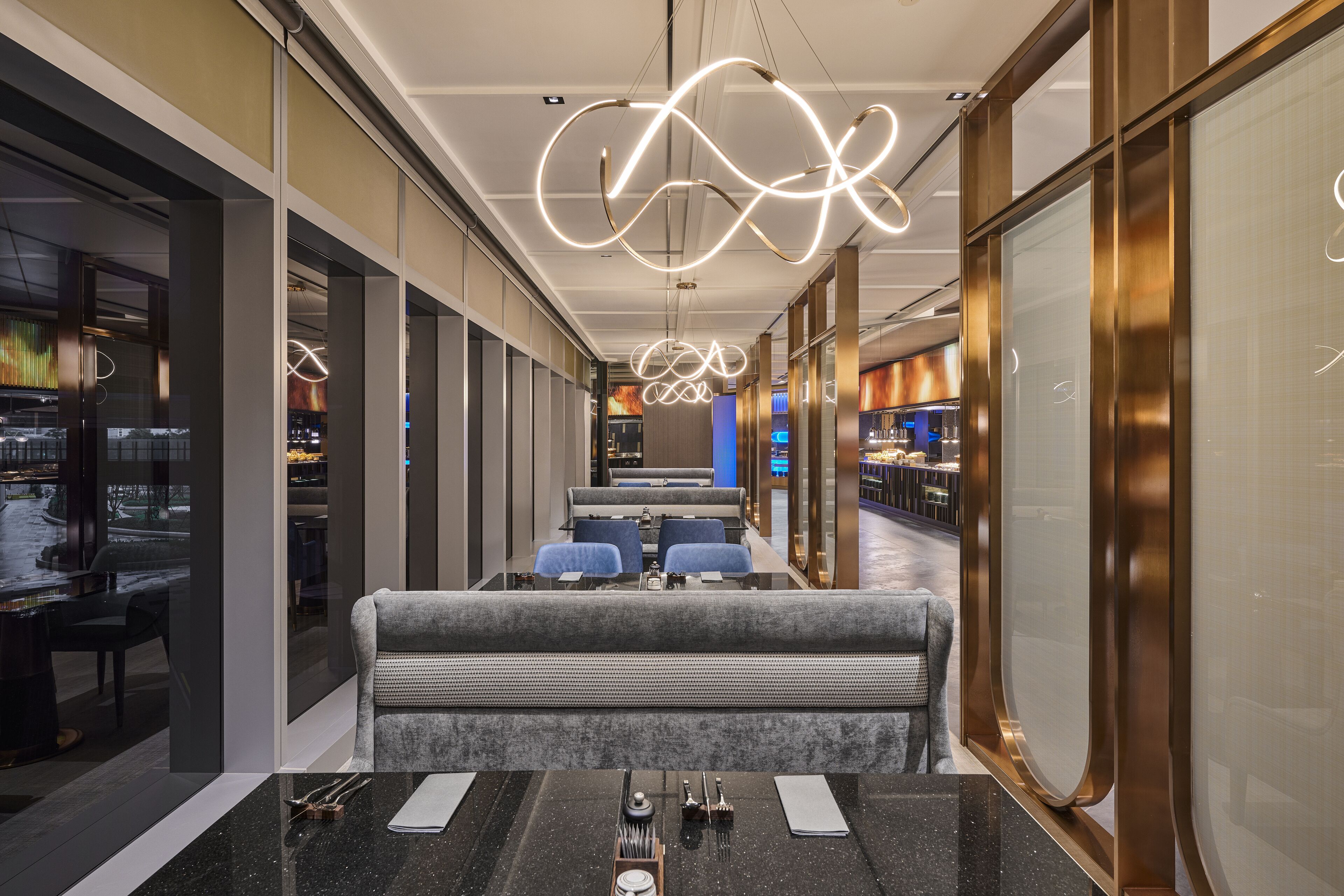 A modern restaurant with a long counter, seating area, and decorative lighting.