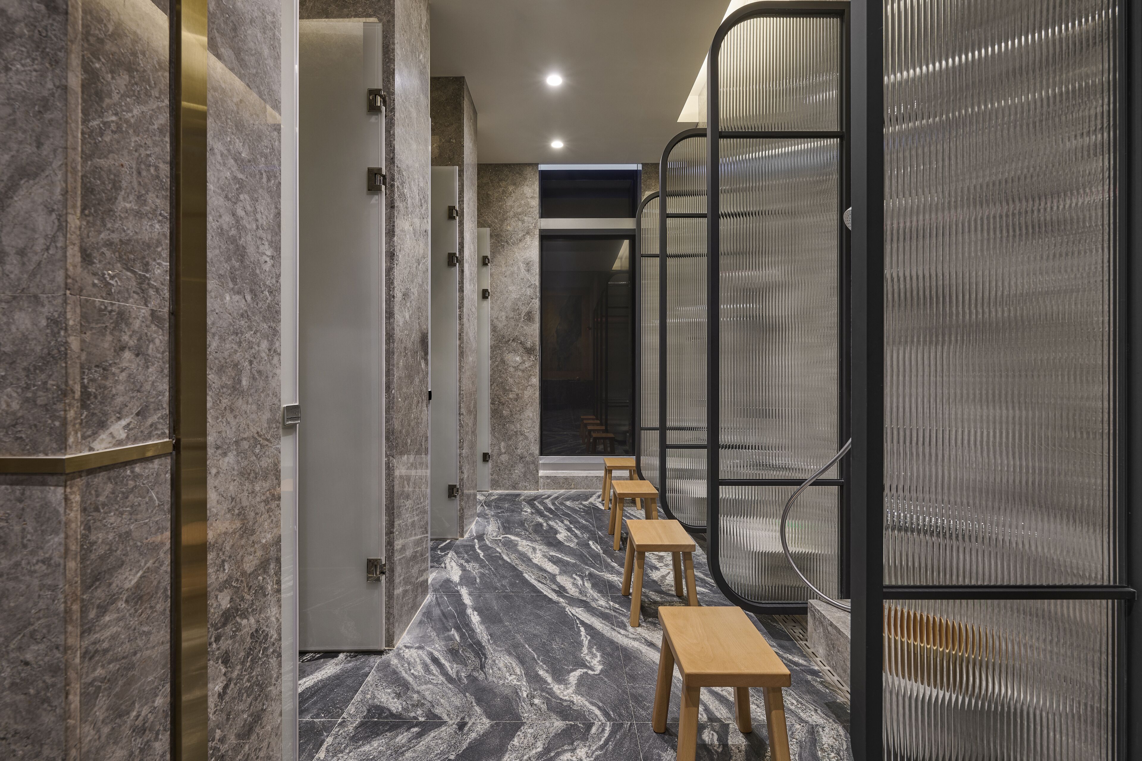 A hallway with marble flooring, wooden benches, and a glass partition.