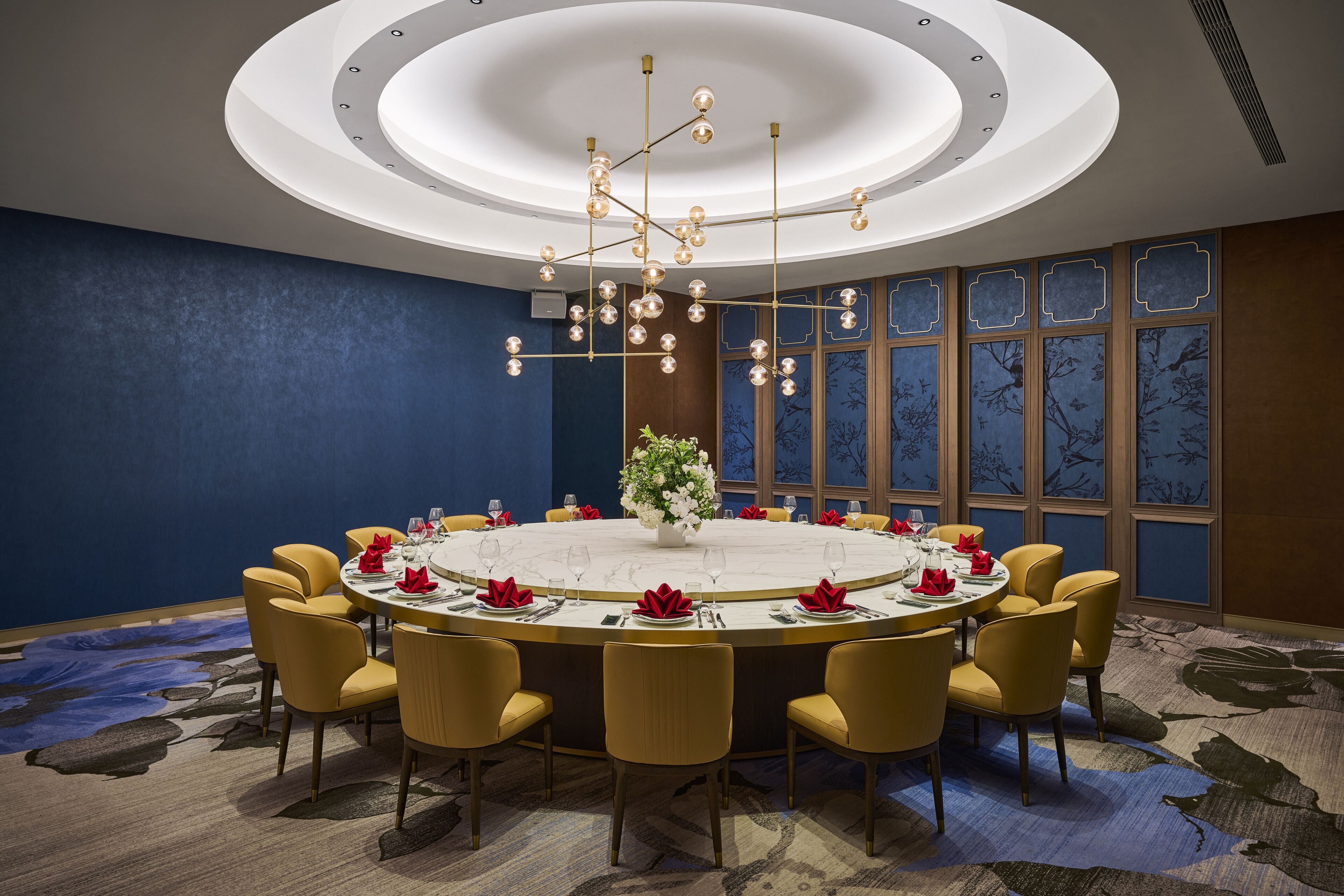A conference room with a round table, yellow chairs, a chandelier, and a decorative vase.