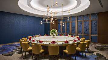A conference room with a round table, yellow chairs, a chandelier, and a decorative vase.