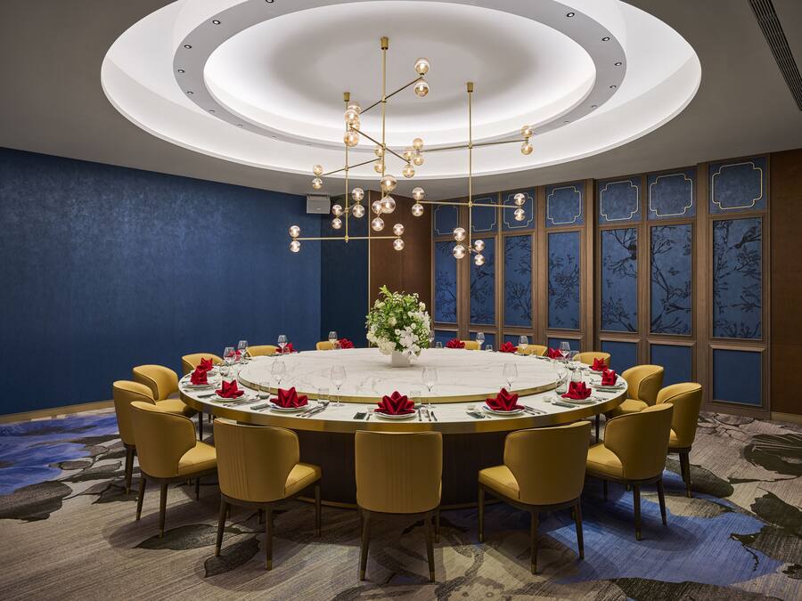 A conference room with a round table, yellow chairs, a chandelier, and a decorative vase.