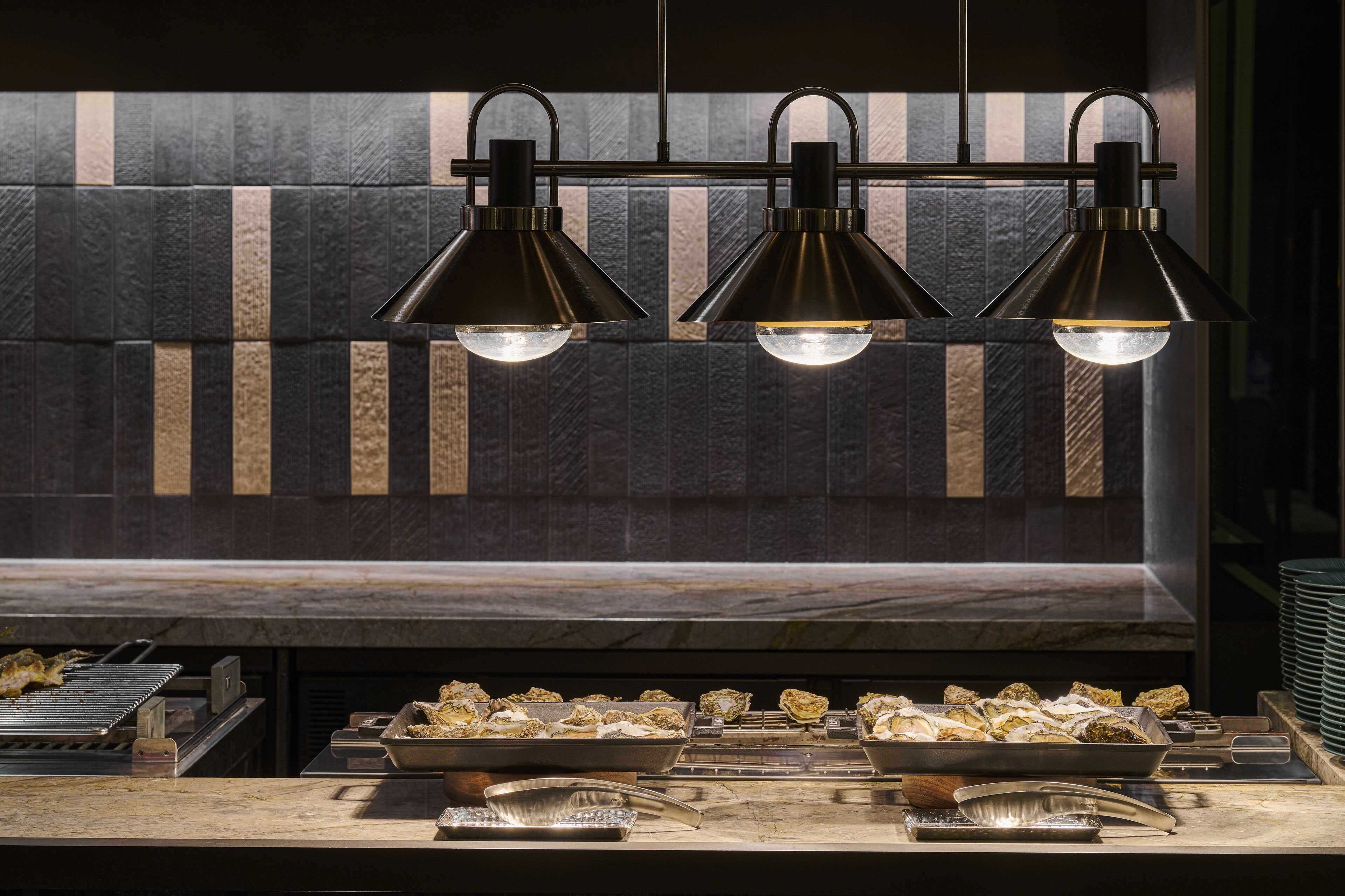 Un restaurante de diseño moderno, con una barra alargada que exhibe alimentos e iluminación colgante.