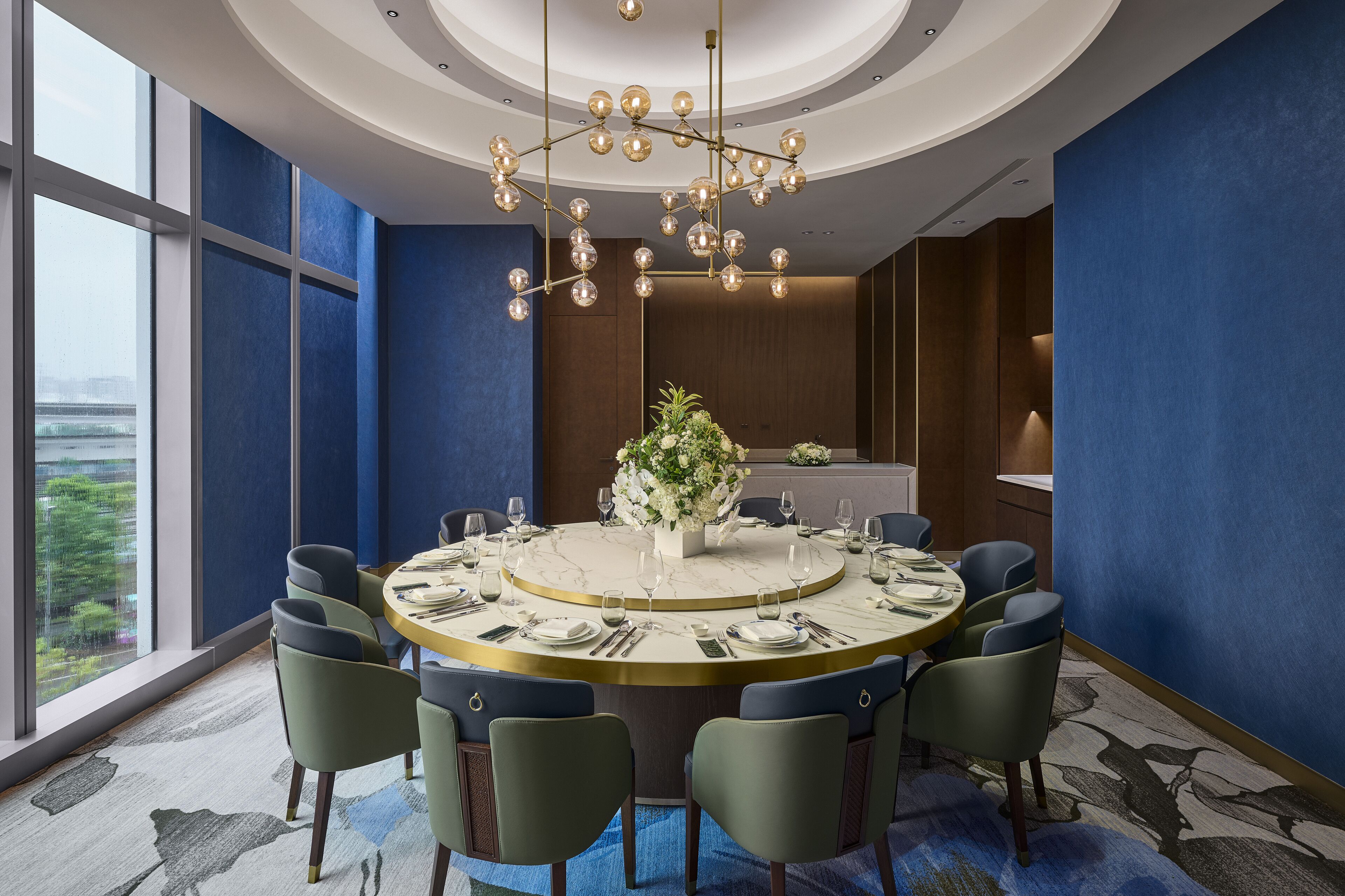A modern dining area with a round table, chairs, and a chandelier.