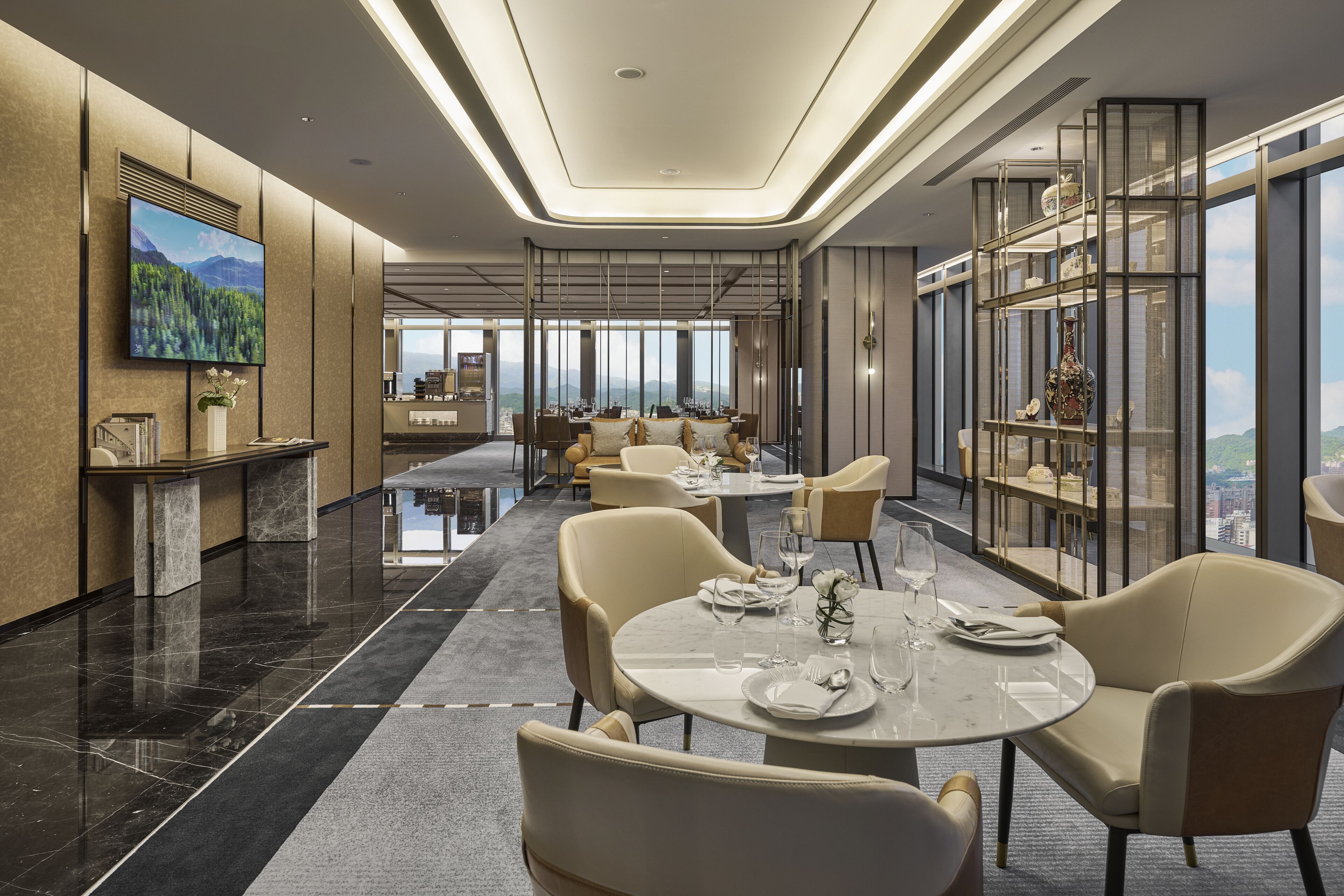 A modern dining area with round tables, beige chairs, and a large TV on the wall.