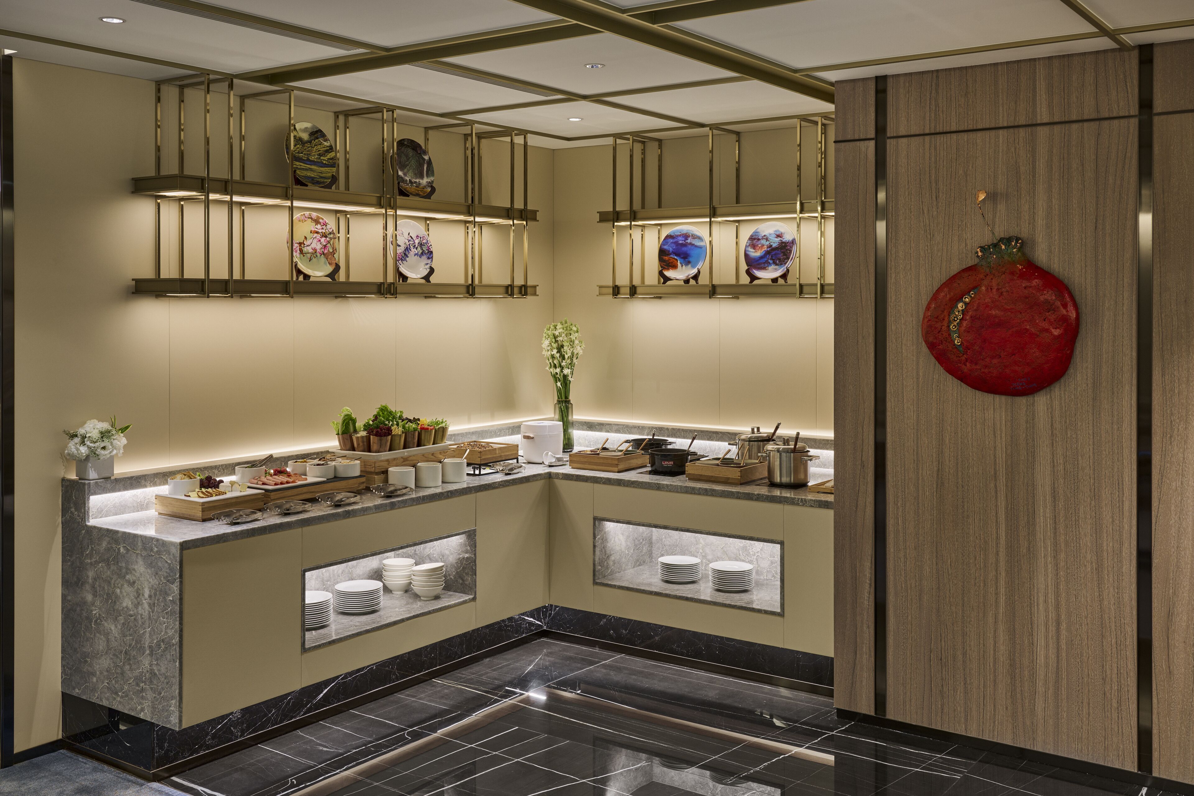 A modern kitchen with marble countertops, built-in shelves displaying decorative plates, and a central island with a vase of flowers.