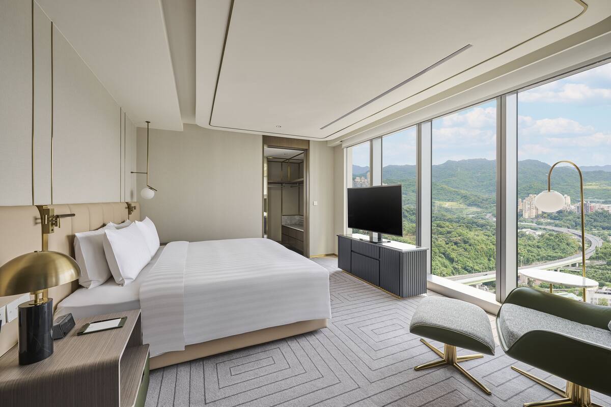 A modern hotel room with a large bed, a TV, and a view of the city.