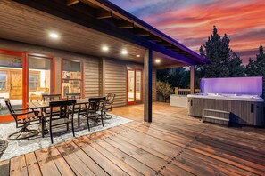 Una terraza de madera con un jacuzzi, asientos al aire libre y un área cubierta con vistas al atardecer.