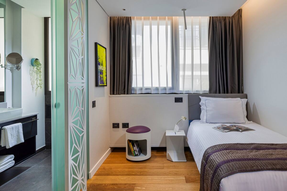 A modern bedroom with a bed, bedside table, and a window with curtains.