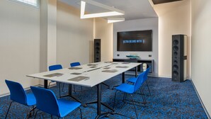 A conference room with a large table, blue chairs, a flat-screen TV, and speakers. - Ultra Ben Yehuda (Tel Aviv)