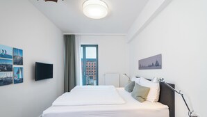 Habitación de hotel con una cama grande, un televisor de pantalla plana, un escritorio con lámpara y una ventana con vistas a edificios.