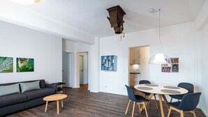 Una sala de estar moderna con un sofá gris oscuro, una mesa de centro redonda de madera y un comedor con una mesa blanca y sillas azules.