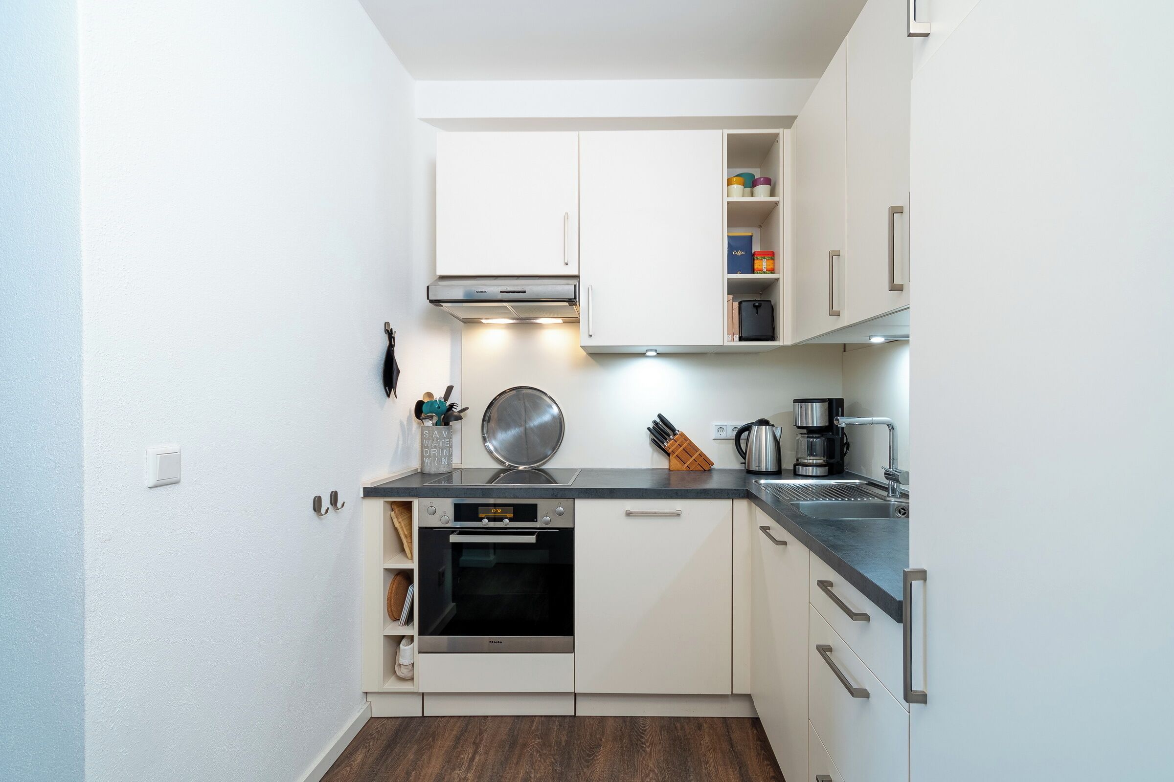 A compact kitchen with white cabinets, a built-in oven, and a coffee maker.