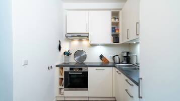 A compact kitchen with white cabinets, a built-in oven, and a coffee maker.