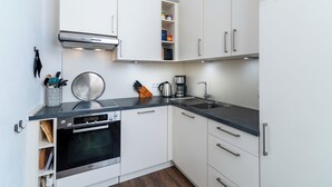 Una cocina compacta con armarios blancos, horno de acero inoxidable, cafetera y un lavabo.