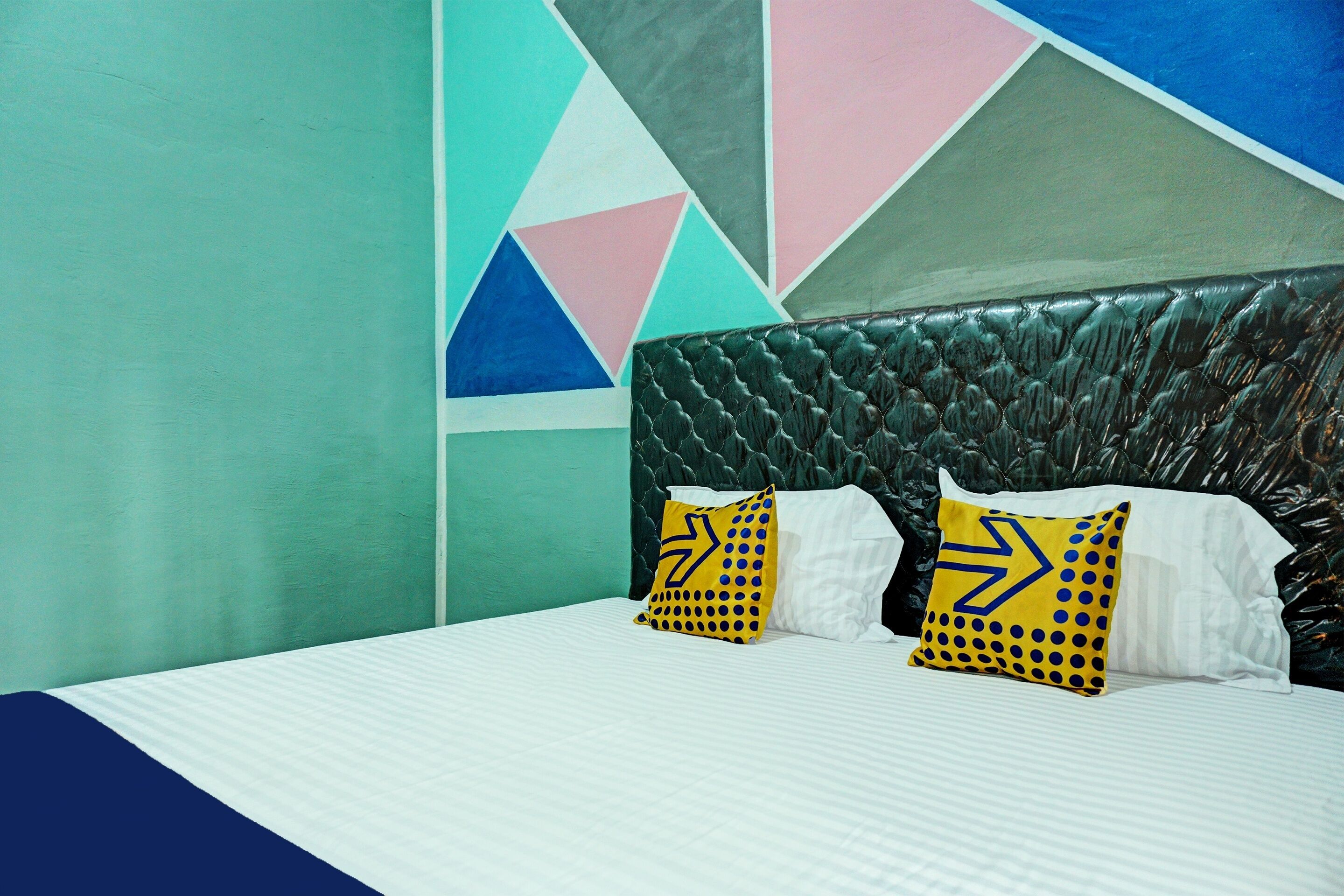 Un letto con biancheria bianca, due cuscini decorati con motivi gialli e neri, e un disegno geometrico sulla parete.